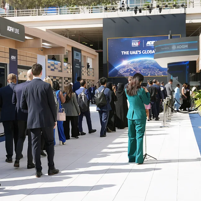 Attendees walking the ADFW Live concourse past the ADGM stage
